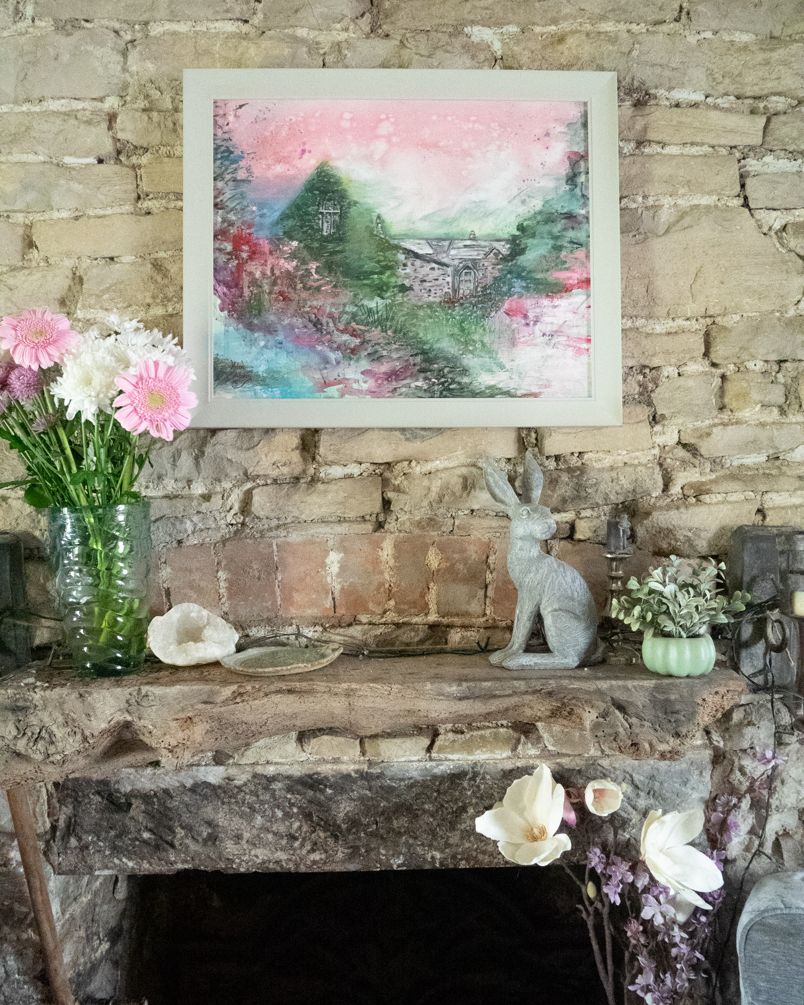 A pretty painting of a gardener's cottage in a garden full of flowers. The colours are pink and green.