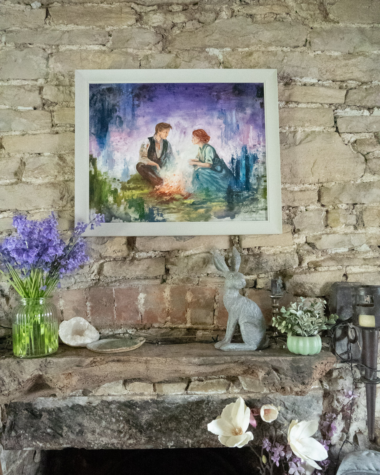 A painting of a couple sitting by an open fire and talking. It is blue, violet and green and feels like it's from a fairytale.